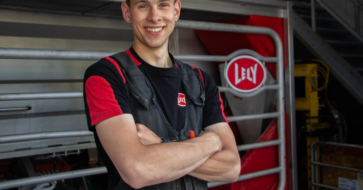 Jonge Lely-monteur lacht met de armen over elkaar naast een machine met Lely-logo